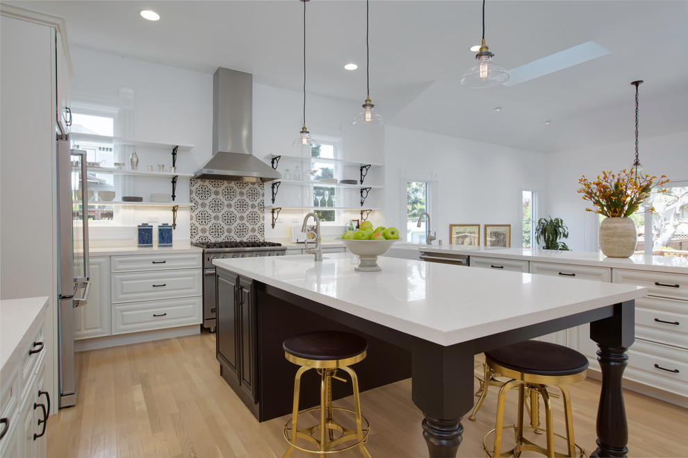 This is an example of a medium sized traditional u-shaped kitchen in San Francisco with a belfast sink, raised-panel cabinets, white cabinets, limestone worktops, white splashback, stainless steel appliances, light hardwood flooring, an island and beige floors.