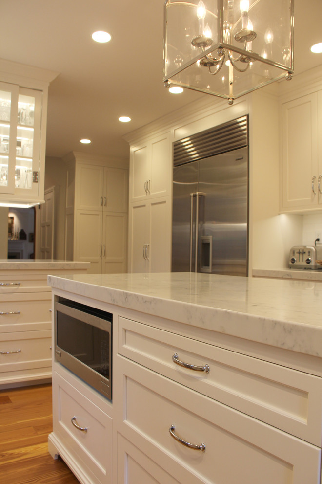 Bild på ett mellanstort vintage u-kök, med en undermonterad diskho, luckor med infälld panel, vita skåp, bänkskiva i kvarts, vitt stänkskydd, stänkskydd i tunnelbanekakel, rostfria vitvaror, mellanmörkt trägolv och en köksö