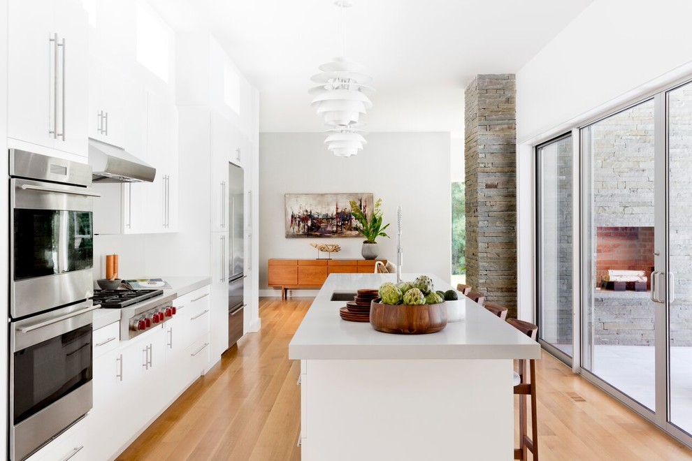 Immagine di una cucina minimalista con lavello sottopiano, ante lisce, ante bianche, elettrodomestici in acciaio inossidabile, pavimento in legno massello medio e pavimento beige