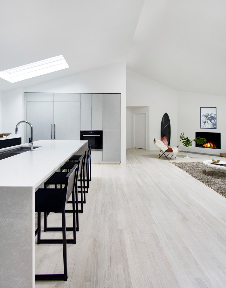 This is an example of a medium sized modern l-shaped open plan kitchen in New York with a double-bowl sink, flat-panel cabinets, grey cabinets, engineered stone countertops, integrated appliances, light hardwood flooring, an island and white floors.