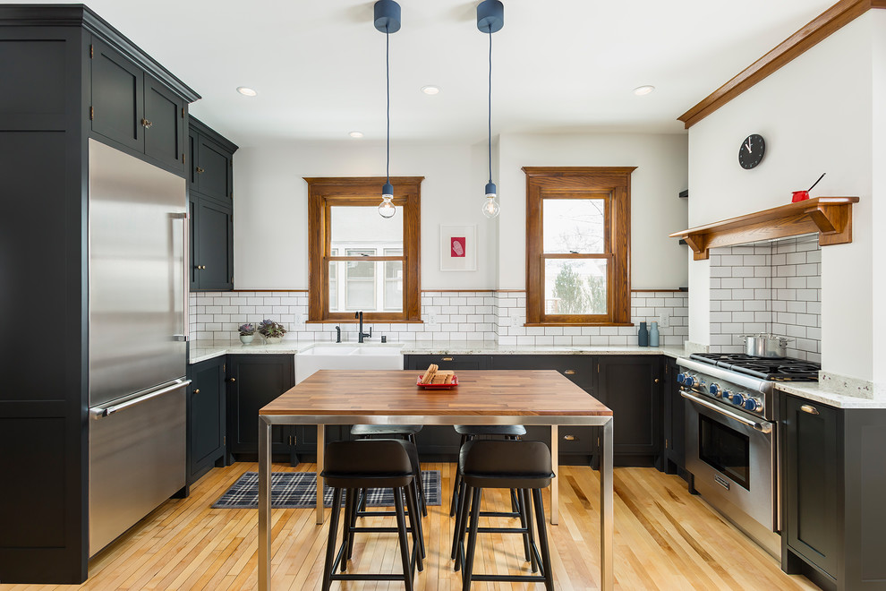 Urige Küche in U-Form mit Landhausspüle, Schrankfronten im Shaker-Stil, schwarzen Schränken, Küchenrückwand in Weiß, Rückwand aus Metrofliesen, hellem Holzboden, Kücheninsel, braunem Boden und grauer Arbeitsplatte in Minneapolis