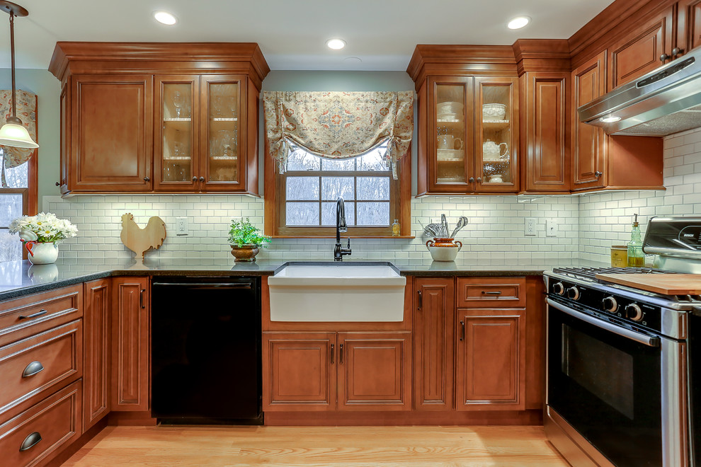 Exempel på ett avskilt, mellanstort lantligt u-kök, med en rustik diskho, skåp i mellenmörkt trä, vitt stänkskydd, stänkskydd i tunnelbanekakel, rostfria vitvaror, ljust trägolv, en halv köksö, granitbänkskiva och luckor med infälld panel