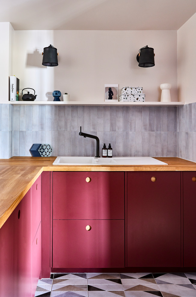ロンドンにあるコンテンポラリースタイルのおしゃれなL型キッチン (ドロップインシンク、フラットパネル扉のキャビネット、赤いキャビネット、木材カウンター、グレーのキッチンパネル、マルチカラーの床、茶色いキッチンカウンター) の写真