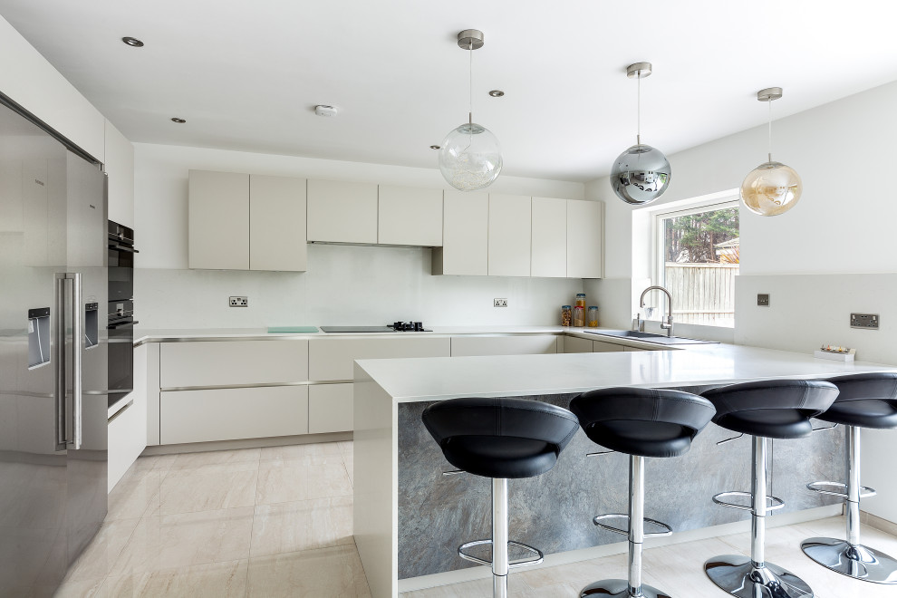 Inspiration for a contemporary u-shaped kitchen in London with a built-in sink, flat-panel cabinets, beige cabinets, white splashback, stainless steel appliances, a breakfast bar, beige floors and white worktops.