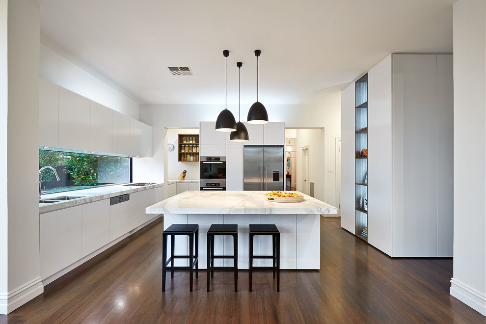 Moderne Küche in U-Form mit Doppelwaschbecken, flächenbündigen Schrankfronten, weißen Schränken, Küchengeräten aus Edelstahl, dunklem Holzboden und Kücheninsel in Melbourne