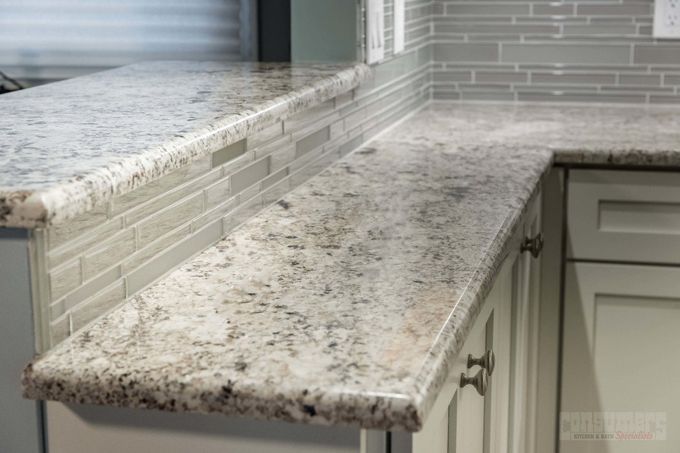 Example of a large galley plywood floor eat-in kitchen design in New York with a farmhouse sink, recessed-panel cabinets, white cabinets, granite countertops, gray backsplash, stainless steel appliances and a peninsula