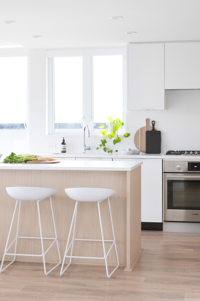 Idee per una cucina contemporanea con ante lisce, ante bianche, elettrodomestici in acciaio inossidabile, parquet chiaro, pavimento marrone e top bianco