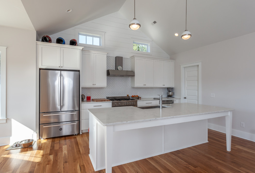 Example of a mid-sized beach style u-shaped medium tone wood floor and brown floor open concept kitchen design in Charleston with a farmhouse sink, shaker cabinets, white cabinets, quartz countertops, white backsplash, stainless steel appliances, an island, white countertops and ceramic backsplash