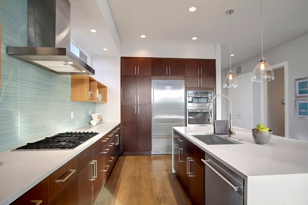 Large contemporary l-shaped open plan kitchen in Seattle with a single-bowl sink, flat-panel cabinets, dark wood cabinets, composite countertops, blue splashback, porcelain splashback, stainless steel appliances, medium hardwood flooring and an island.