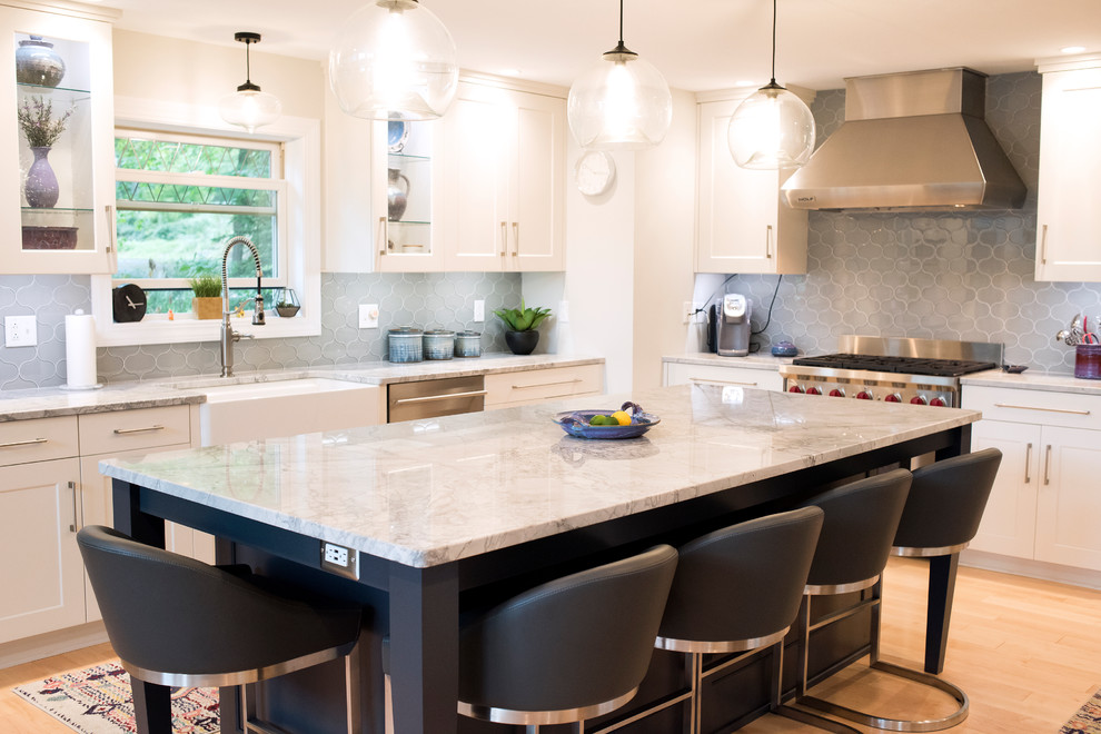 Large transitional u-shaped light wood floor open concept kitchen photo in New York with a farmhouse sink, flat-panel cabinets, white cabinets, quartzite countertops, gray backsplash, ceramic backsplash, stainless steel appliances, an island and gray countertops