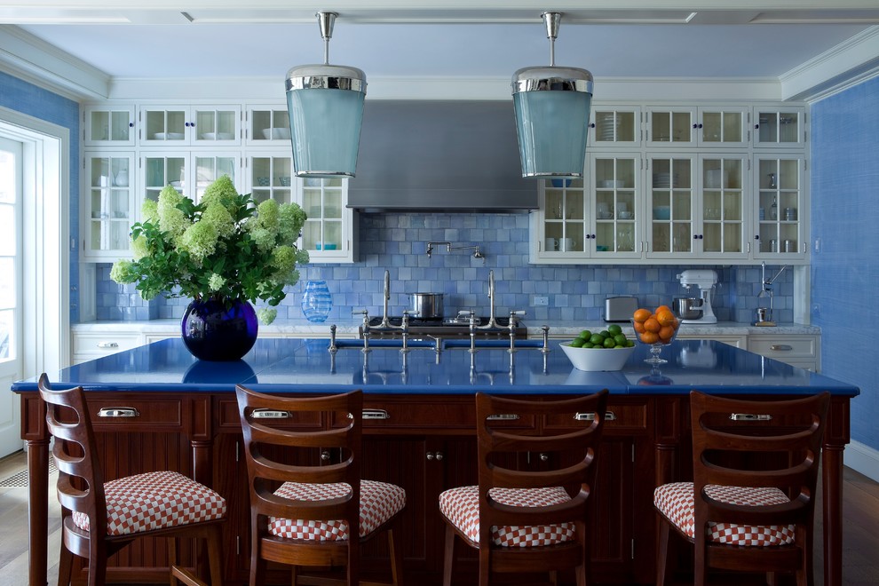 Exemple d'une cuisine parallèle chic avec un évier encastré, un placard à porte vitrée, des portes de placard blanches, une crédence bleue, un électroménager en acier inoxydable, un sol en bois brun, îlot et un plan de travail bleu.