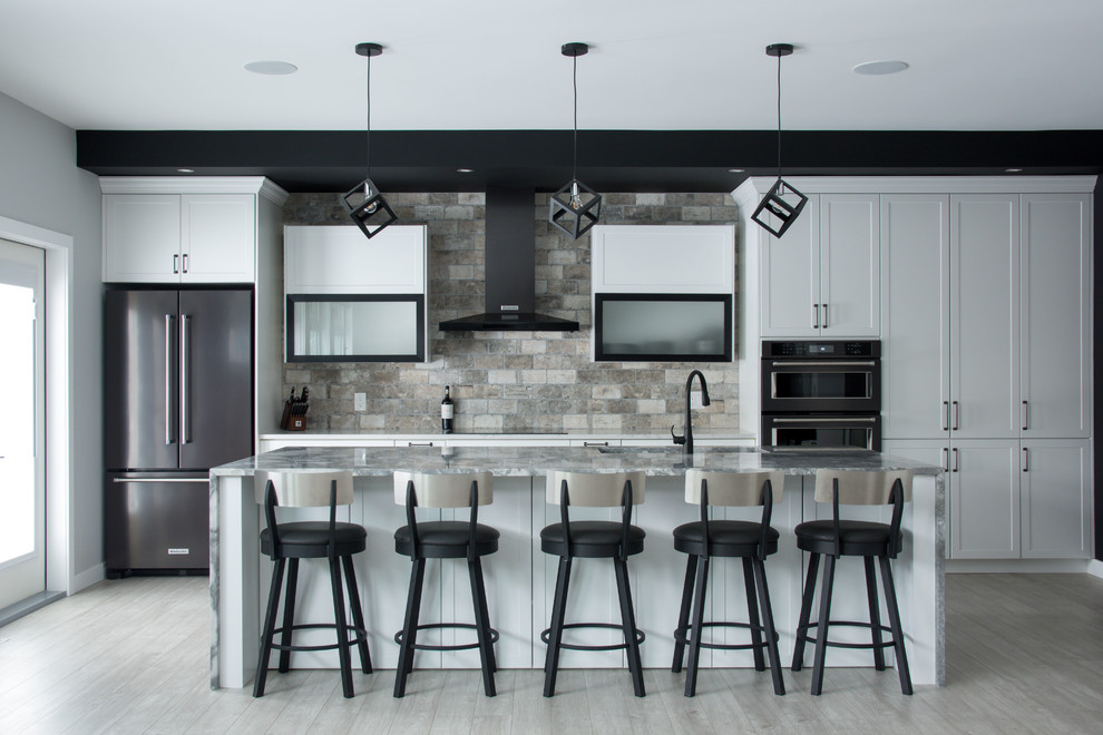 Inredning av ett modernt mellanstort grå grått kök, med en undermonterad diskho, skåp i shakerstil, vita skåp, granitbänkskiva, grått stänkskydd, stänkskydd i travertin, svarta vitvaror, laminatgolv, en köksö och grått golv