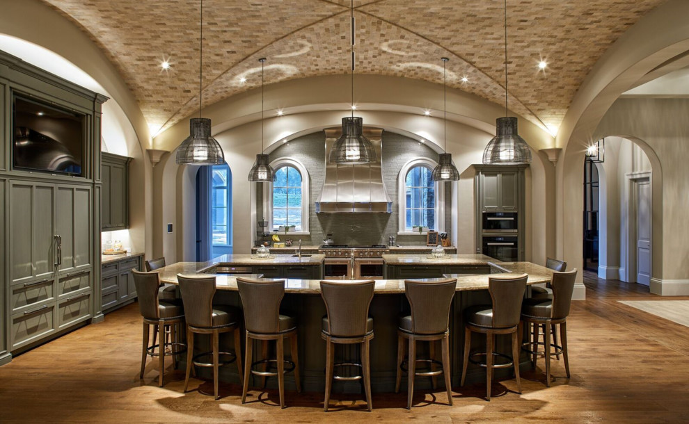 Kitchen - traditional l-shaped medium tone wood floor and brown floor kitchen idea in Houston with an undermount sink, recessed-panel cabinets, green cabinets, gray backsplash, black appliances, two islands and beige countertops