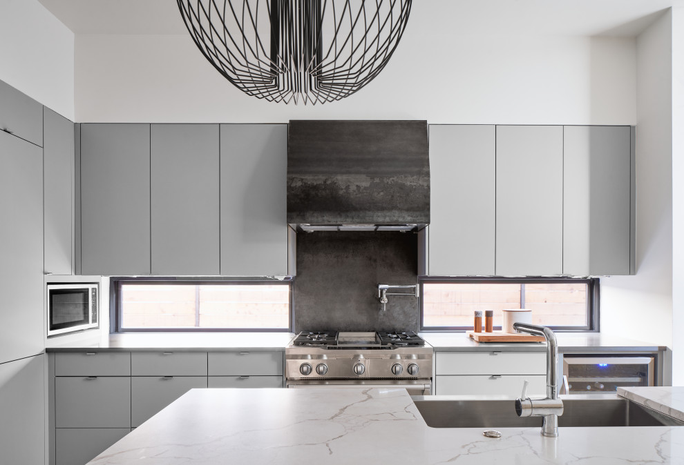 Inredning av ett modernt litet grå grått l-kök, med en rustik diskho, släta luckor, grå skåp, bänkskiva i kvarts, rostfria vitvaror, en köksö och fönster som stänkskydd