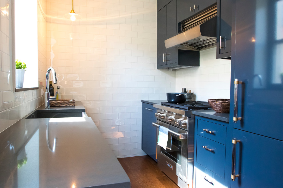 Example of a small minimalist galley medium tone wood floor kitchen design in New York with an integrated sink, flat-panel cabinets, blue cabinets, quartz countertops, white backsplash, subway tile backsplash and stainless steel appliances