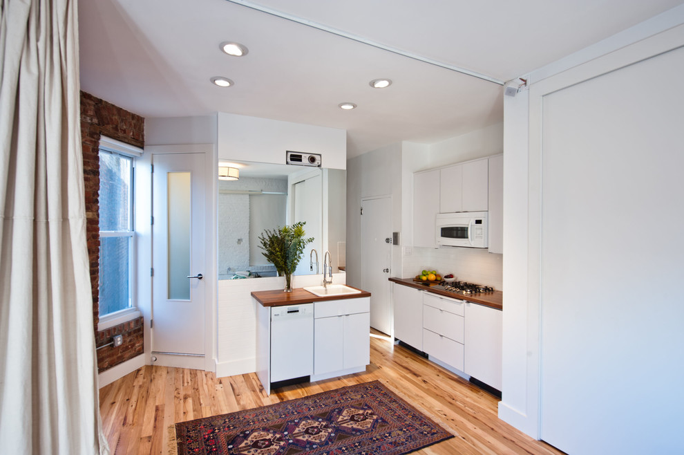 Moderne Küche mit Arbeitsplatte aus Holz, Einbauwaschbecken, flächenbündigen Schrankfronten, weißen Schränken, Küchenrückwand in Weiß, Rückwand aus Metrofliesen und weißen Elektrogeräten in New York