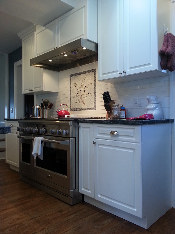 Klassisk inredning av ett kök, med en undermonterad diskho, skåp i shakerstil, vita skåp, granitbänkskiva, vitt stänkskydd, stänkskydd i mosaik, rostfria vitvaror, mellanmörkt trägolv, en köksö och brunt golv