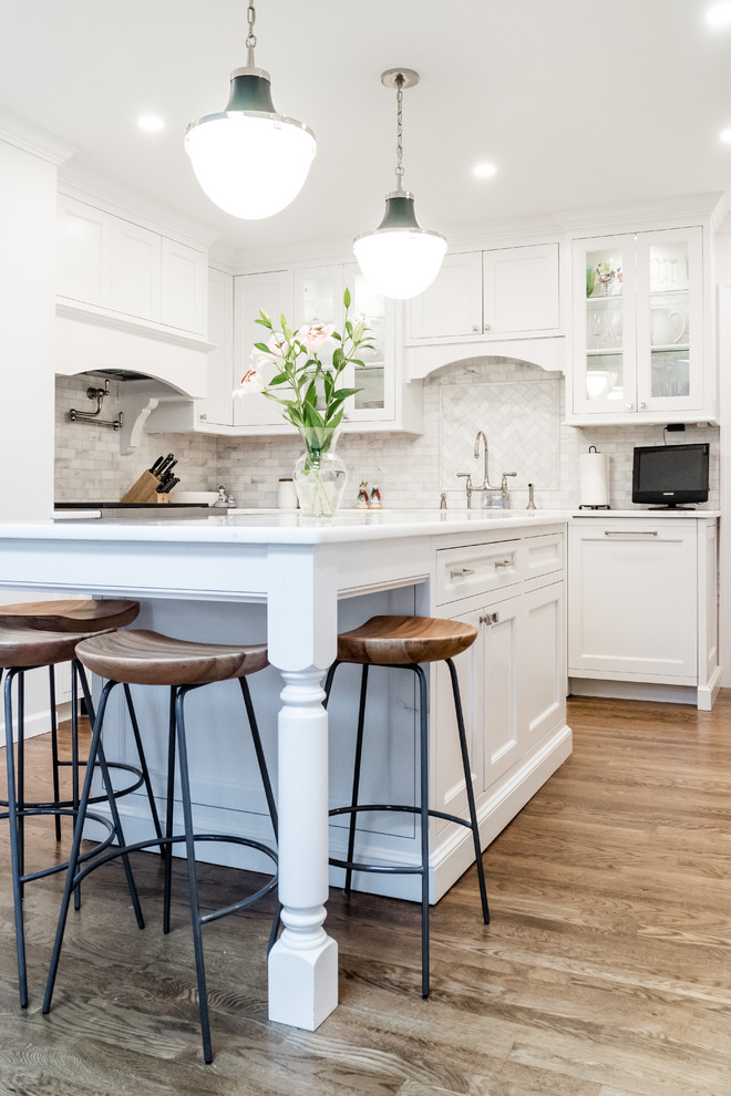 Inspiration for a small traditional u-shaped kitchen in New York with a belfast sink, recessed-panel cabinets, white cabinets, quartz worktops, grey splashback, marble splashback, integrated appliances, dark hardwood flooring, an island, brown floors and white worktops.