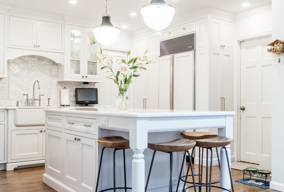 Klassisk inredning av ett litet vit vitt u-kök, med en rustik diskho, luckor med infälld panel, vita skåp, bänkskiva i kvartsit, stänkskydd i marmor, integrerade vitvaror, mörkt trägolv, en köksö, brunt golv och vitt stänkskydd
