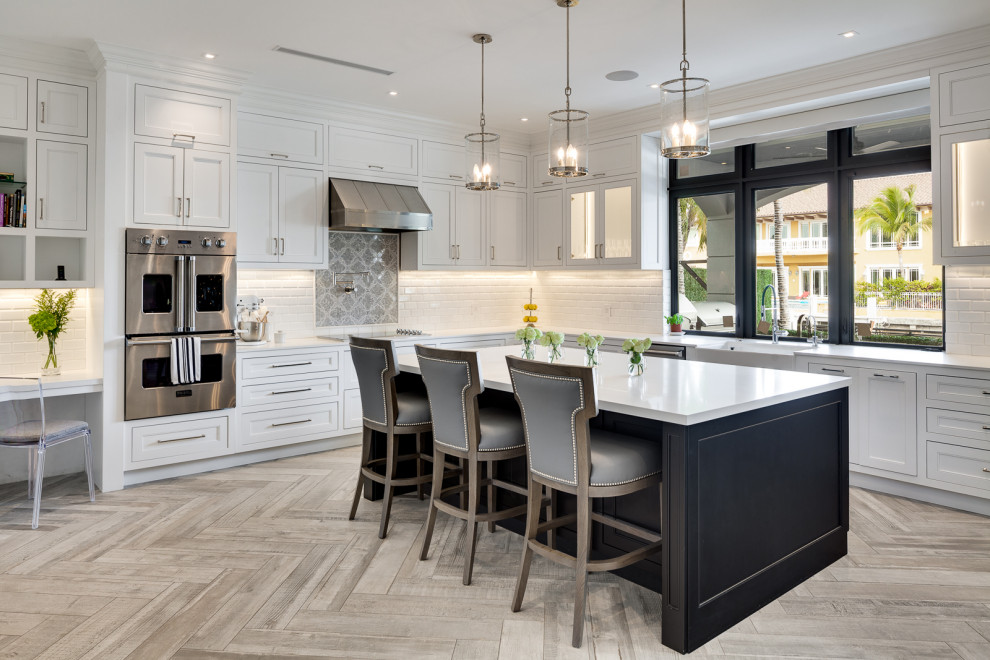 Expansive classic l-shaped kitchen/diner in Miami with a belfast sink, shaker cabinets, white cabinets, engineered stone countertops, white splashback, metro tiled splashback, stainless steel appliances, porcelain flooring, an island, grey floors and white worktops.