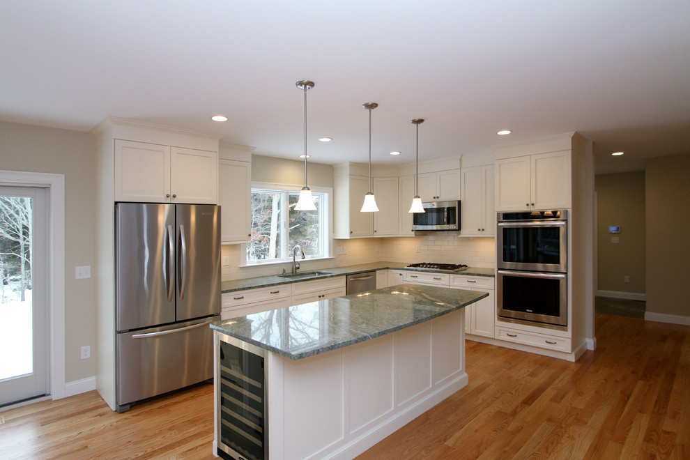 Foto på ett mellanstort funkis kök, med en undermonterad diskho, luckor med infälld panel, vita skåp, granitbänkskiva, stänkskydd i keramik, rostfria vitvaror, mellanmörkt trägolv och en köksö