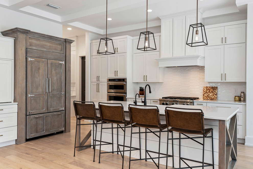 Inspiration for a large transitional l-shaped light wood floor and beige floor kitchen remodel in Orlando with a farmhouse sink, shaker cabinets, white cabinets, marble countertops, white backsplash, stainless steel appliances, an island and white countertops