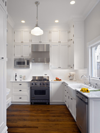 Example of a small classic l-shaped dark wood floor enclosed kitchen design in San Francisco with a farmhouse sink, recessed-panel cabinets, white cabinets, marble countertops, white backsplash, ceramic backsplash, stainless steel appliances and no island