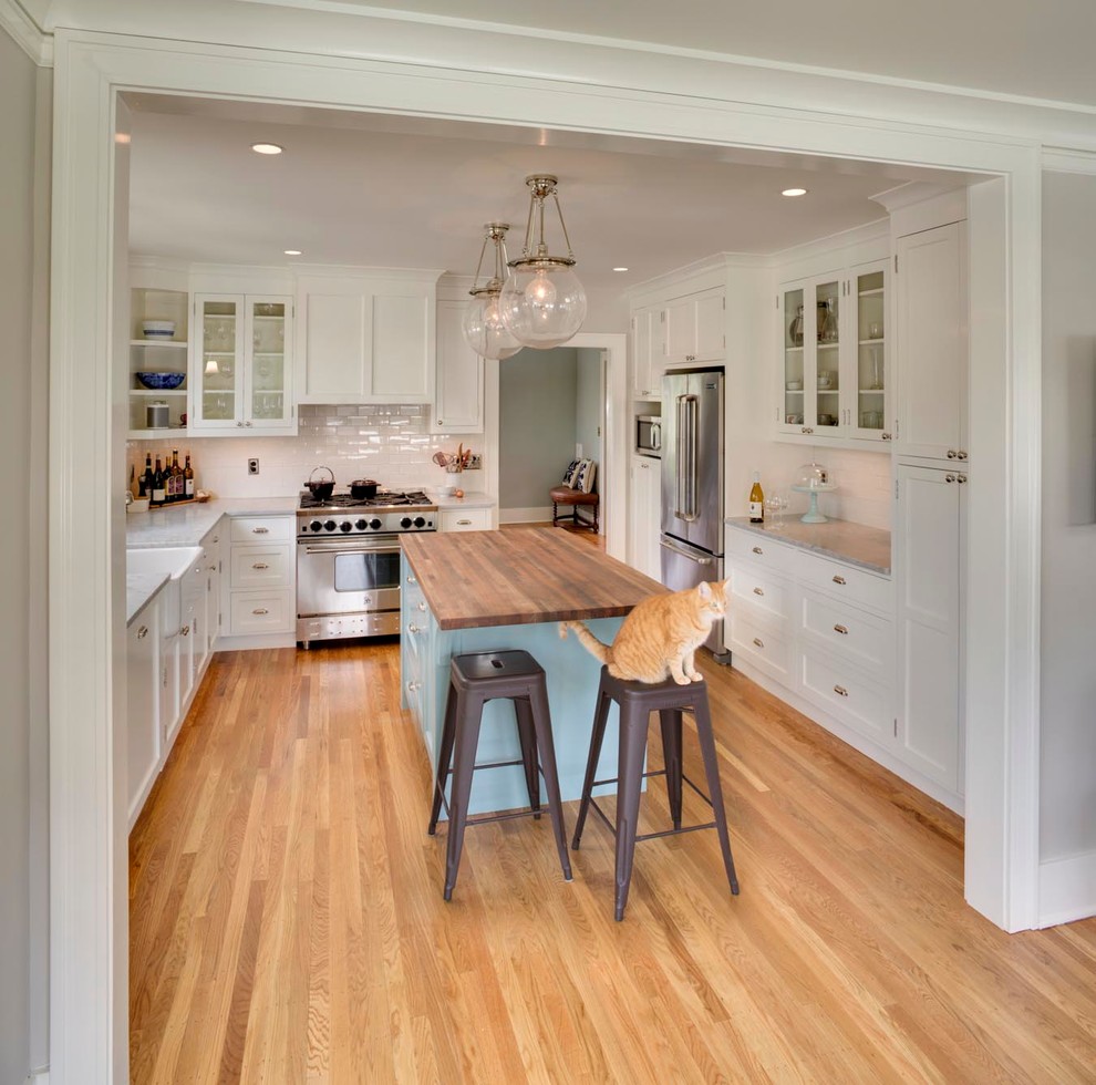Mid-sized arts and crafts u-shaped medium tone wood floor eat-in kitchen photo in Portland with a farmhouse sink, shaker cabinets, white cabinets, marble countertops, white backsplash, subway tile backsplash, stainless steel appliances and an island