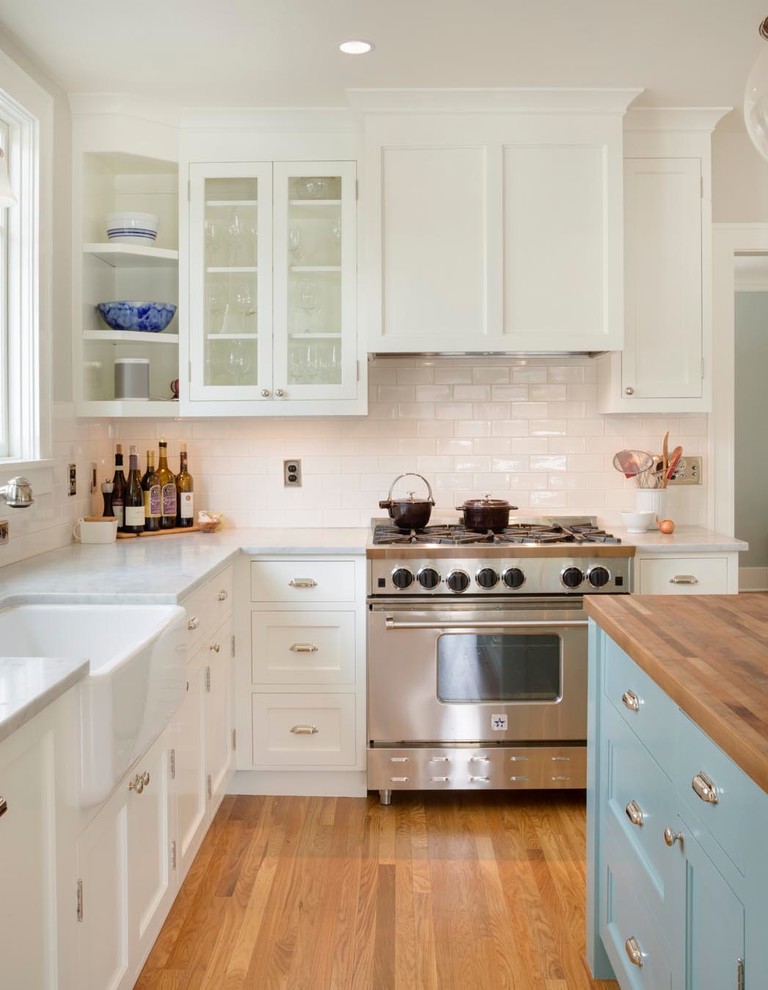 Eat-in kitchen - mid-sized traditional u-shaped medium tone wood floor eat-in kitchen idea in Portland with a farmhouse sink, shaker cabinets, white cabinets, marble countertops, white backsplash, subway tile backsplash, stainless steel appliances and an island