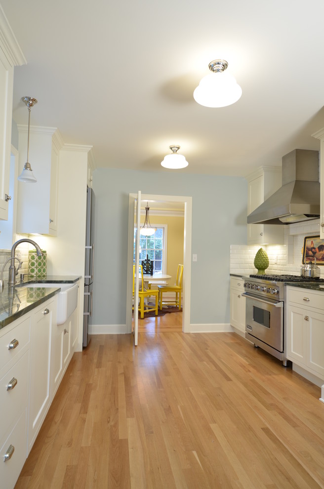 Example of a mid-sized arts and crafts galley light wood floor eat-in kitchen design in Portland with a farmhouse sink, shaker cabinets, white cabinets, granite countertops, white backsplash, ceramic backsplash, stainless steel appliances and no island