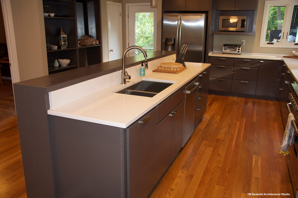 Foto på ett avskilt, mellanstort funkis l-kök, med en undermonterad diskho, släta luckor, bruna skåp, bänkskiva i kvarts, rostfria vitvaror, mellanmörkt trägolv och en köksö