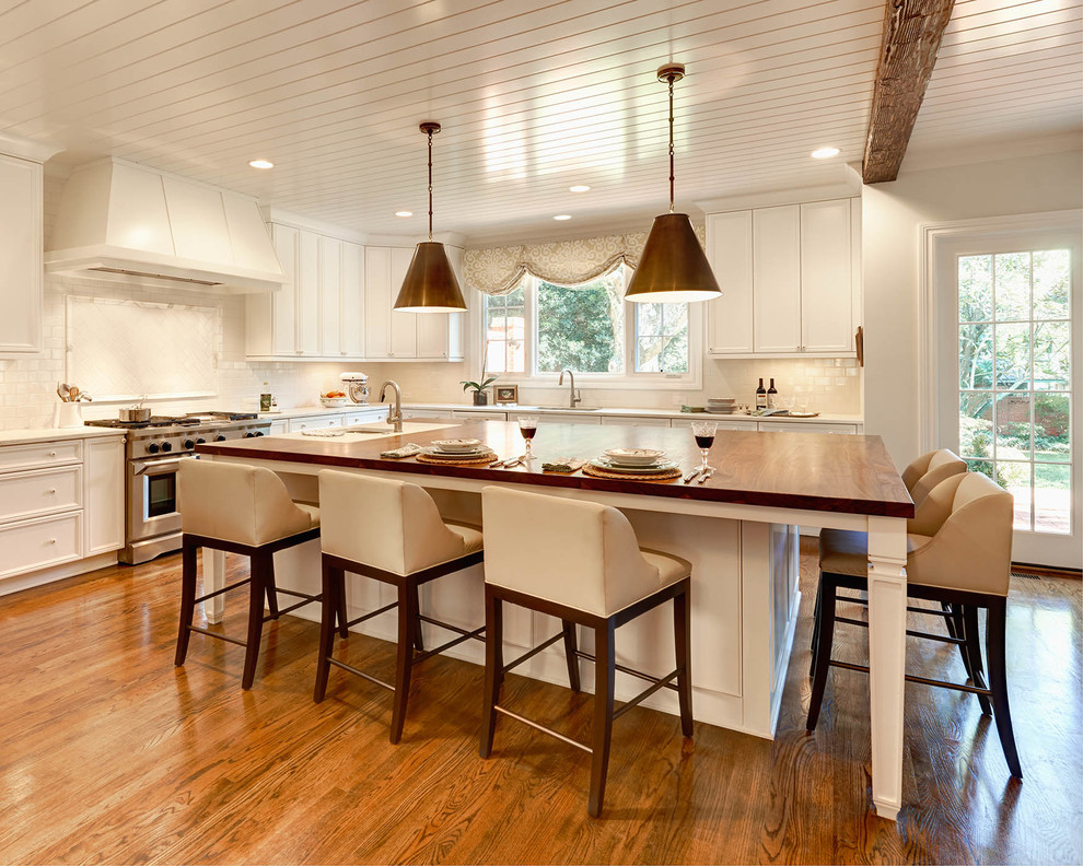 Elegant l-shaped medium tone wood floor kitchen photo in Charlotte with a drop-in sink, recessed-panel cabinets, white cabinets, wood countertops, white backsplash, subway tile backsplash, stainless steel appliances and an island