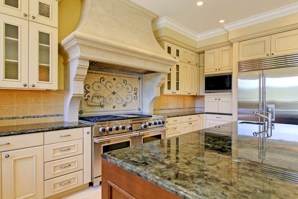 Bild på ett medelhavsstil kök, med en undermonterad diskho, luckor med upphöjd panel, vita skåp, granitbänkskiva, gult stänkskydd, stänkskydd i stenkakel, rostfria vitvaror, kalkstensgolv och en köksö