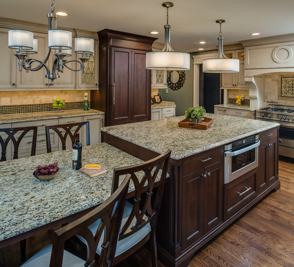 Example of a large classic u-shaped medium tone wood floor eat-in kitchen design in Detroit with an undermount sink, recessed-panel cabinets, distressed cabinets, granite countertops, beige backsplash, subway tile backsplash, stainless steel appliances and an island