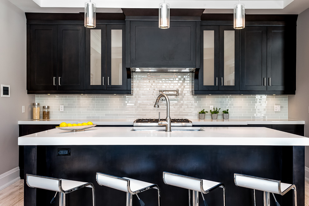 This is an example of a classic kitchen in Toronto with a submerged sink, glass-front cabinets, black cabinets, grey splashback, metro tiled splashback and light hardwood flooring.