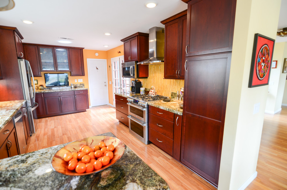 Bild på ett stort funkis kök, med en enkel diskho, luckor med infälld panel, röda skåp, granitbänkskiva, gult stänkskydd, stänkskydd i glaskakel, rostfria vitvaror och mellanmörkt trägolv