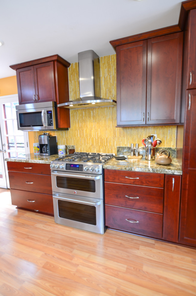 Modern inredning av ett stort kök, med en enkel diskho, luckor med infälld panel, röda skåp, granitbänkskiva, gult stänkskydd, stänkskydd i glaskakel, rostfria vitvaror och mellanmörkt trägolv