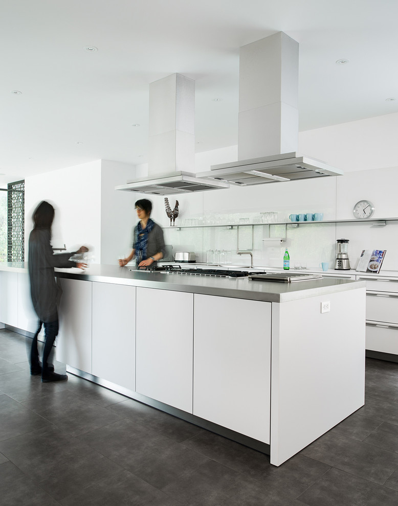 Foto på ett funkis kök, med öppna hyllor, bänkskiva i rostfritt stål, vitt stänkskydd, stänkskydd i glaskakel, rostfria vitvaror, en köksö och betonggolv
