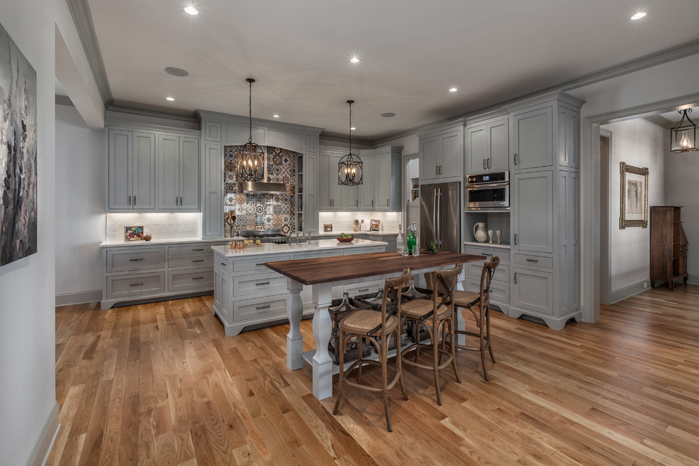 Inspiration for a large timeless l-shaped medium tone wood floor eat-in kitchen remodel in Other with a farmhouse sink, shaker cabinets, gray cabinets, solid surface countertops, multicolored backsplash, porcelain backsplash, stainless steel appliances and two islands