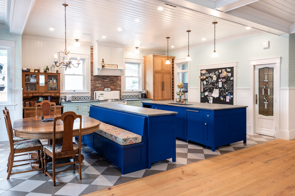 Пример оригинального дизайна: большая п-образная кухня в стиле фьюжн с обеденным столом, фасадами в стиле шейкер, синими фасадами, разноцветным фартуком, фартуком из кирпича, полом из керамогранита, двумя и более островами, разноцветным полом, серой столешницей, врезной мойкой и техникой под мебельный фасад