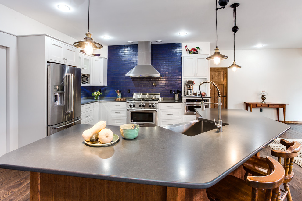 Mid-sized eclectic l-shaped dark wood floor open concept kitchen photo in Providence with a farmhouse sink, beaded inset cabinets, white cabinets, quartz countertops, blue backsplash, brick backsplash, stainless steel appliances and an island