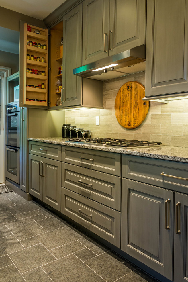 Photo of a small traditional u-shaped enclosed kitchen in Other with a submerged sink, raised-panel cabinets, grey cabinets, engineered stone countertops, grey splashback, porcelain splashback, stainless steel appliances, travertine flooring, a breakfast bar and grey floors.