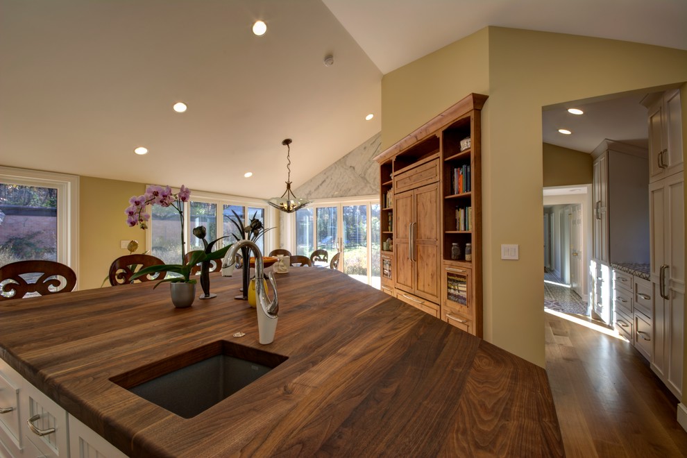 This is an example of a large l-shaped kitchen in Chicago with an island, a submerged sink, white cabinets, white splashback, stone slab splashback and light hardwood flooring.