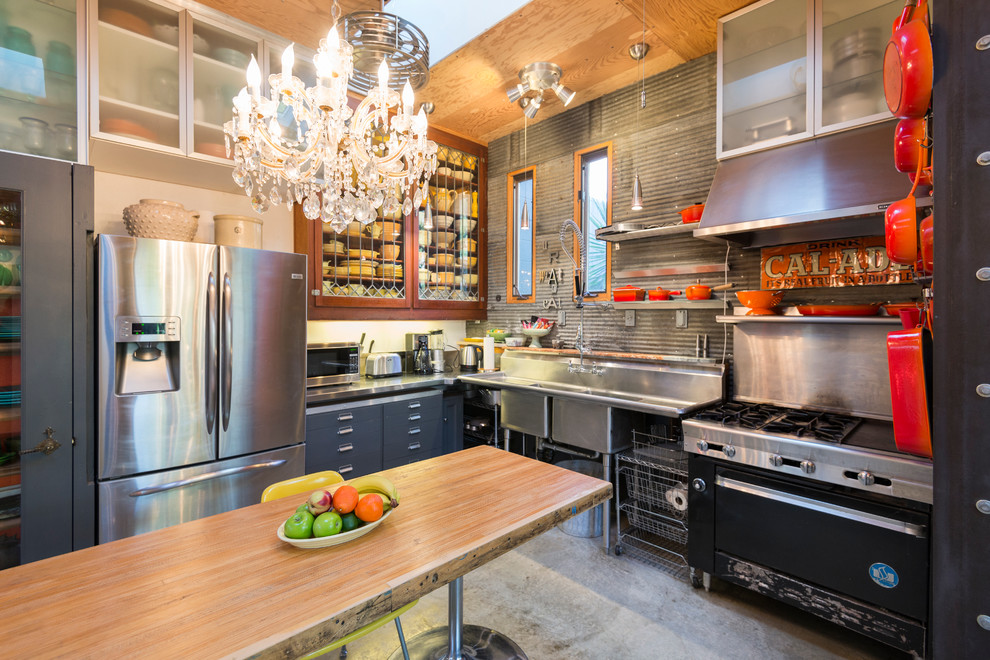 サンフランシスコにあるエクレクティックスタイルのおしゃれなキッチン (ダブルシンク、ガラス扉のキャビネット、ステンレスキャビネット、ステンレスカウンター、メタリックのキッチンパネル、シルバーの調理設備、コンクリートの床) の写真