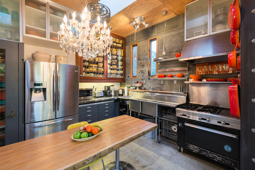 Imagen de cocina bohemia grande con fregadero de doble seno, armarios tipo vitrina, electrodomésticos de acero inoxidable y suelo de cemento