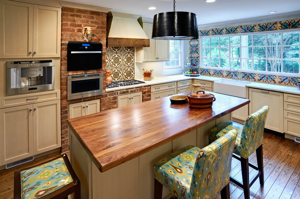 Cette photo montre une cuisine chic en L avec un évier de ferme, un électroménager en acier inoxydable, un plan de travail en bois, un placard à porte shaker et une crédence multicolore.