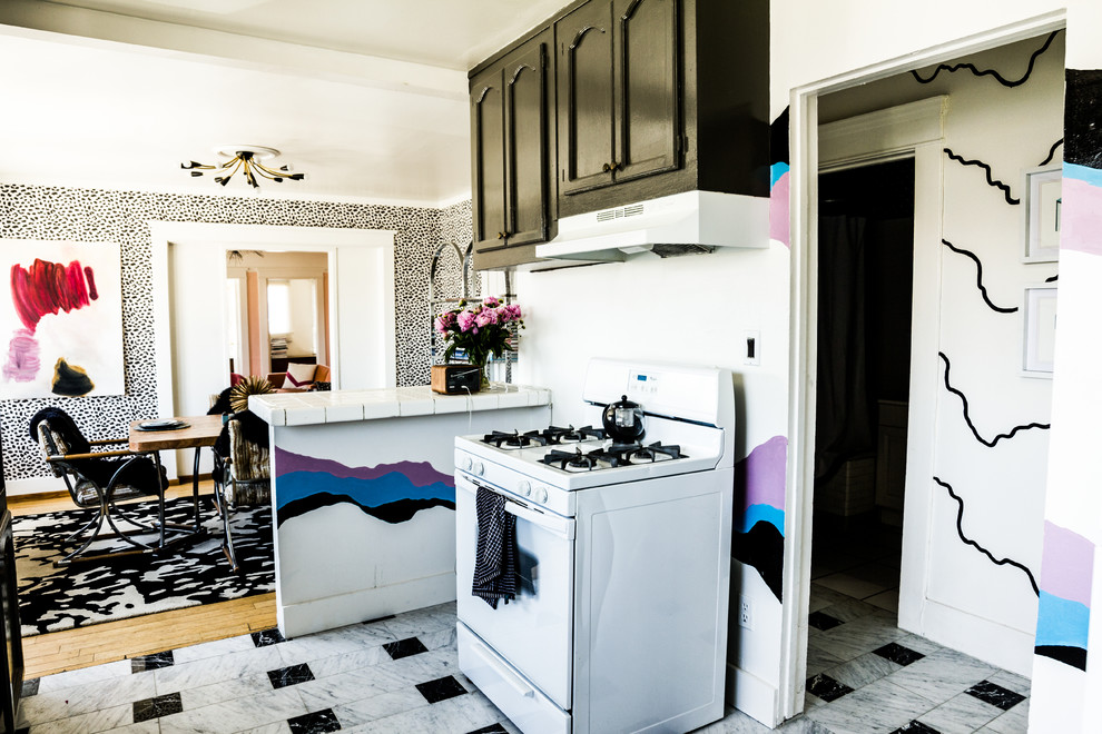 ロサンゼルスにあるエクレクティックスタイルのおしゃれなキッチン (落し込みパネル扉のキャビネット、黒いキャビネット、タイルカウンター、白い調理設備、壁紙) の写真