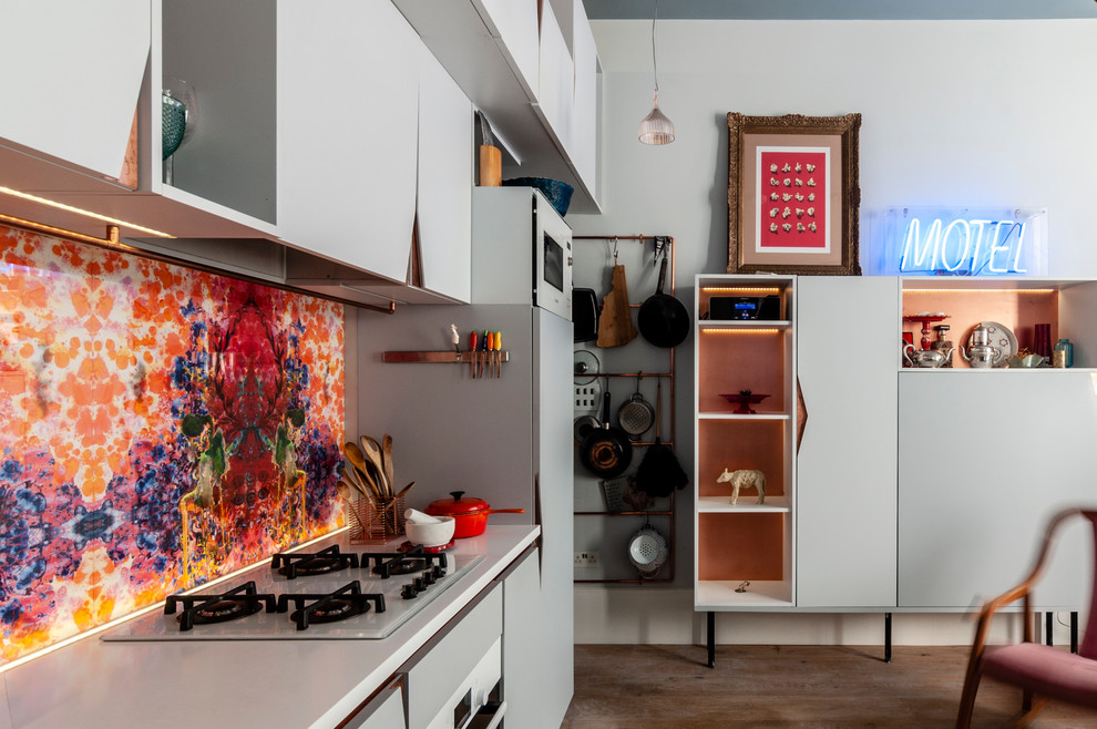 Small bohemian galley kitchen/diner in London with an integrated sink, flat-panel cabinets, grey cabinets, composite countertops, multi-coloured splashback, glass sheet splashback, coloured appliances, medium hardwood flooring, no island, brown floors and white worktops.