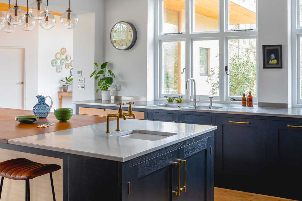Example of an eclectic medium tone wood floor kitchen design in Oxfordshire with shaker cabinets, blue cabinets, stainless steel countertops, stainless steel appliances and an island