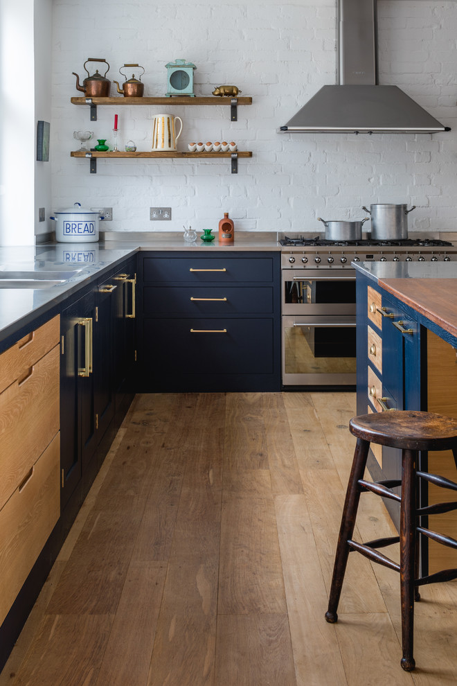 Esempio di un cucina con isola centrale eclettico con ante in stile shaker, ante blu, top in acciaio inossidabile, elettrodomestici in acciaio inossidabile e pavimento in legno massello medio